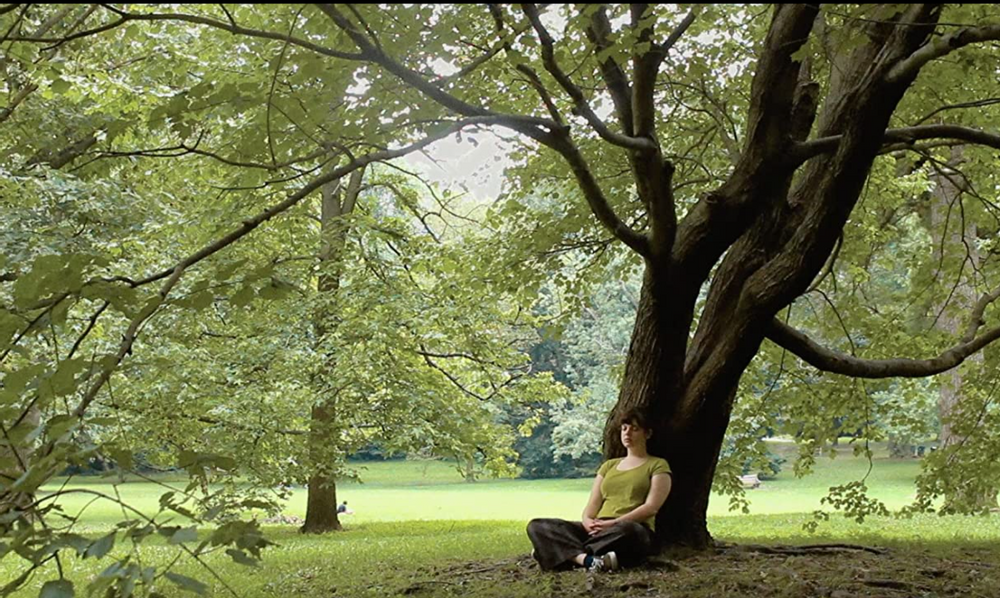 Still image from Kaleidoscope in which Grace Conley's character sits by a tree.