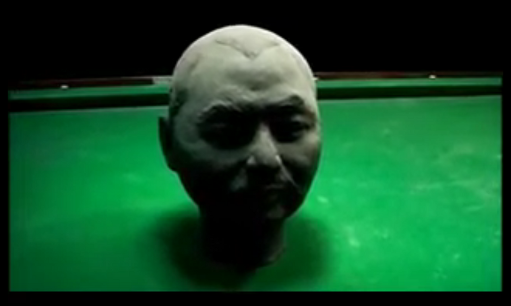 A clay sculpture of a man's head sits in the middle of a pool table.