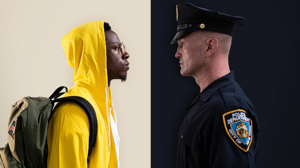 The image is split in two - the left sports a white background and the right a navy one. An officer stands the right, facing the man who stands in a bright yellow hoodie on the left. 